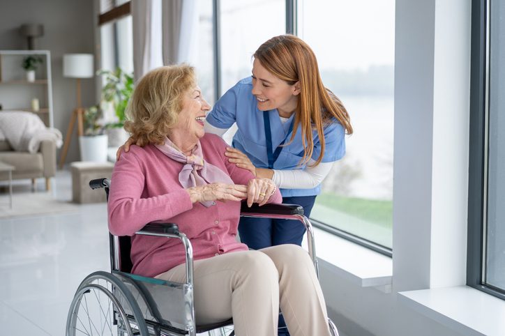 An elderly woman in a wheelchair shares a smile with her nurse, reflecting the joy and support found in compassionate healthcare.