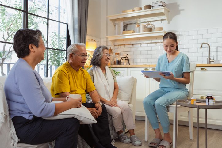 Healthy Asian senior couple receives compassionate healthcare consultation as professional doctor and nurse discuss personalized treatment plan and wellness monitoring in comfortable nursing home environment