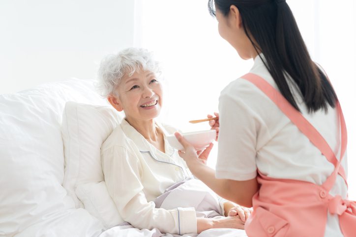 A female caregiver caring for a senior woman sleeping in bed